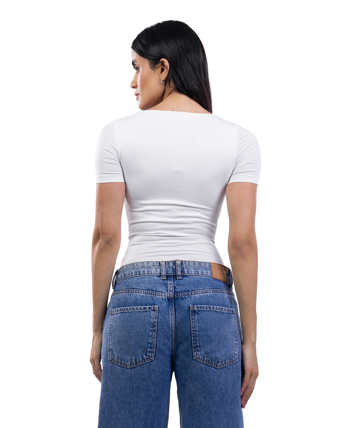 A woman shown from the back wearing a fitted white short-sleeve top and blue jeans against a plain white studio background.