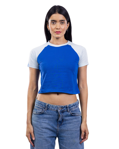 A woman modeling a short-sleeve raglan crop top with a bright blue body and white sleeves, paired with blue jeans, against a plain white background.