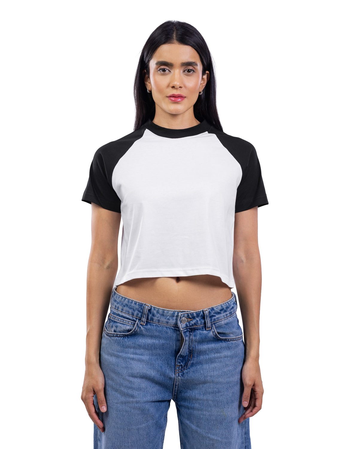 A woman modeling a short-sleeve crop top with a white body and black raglan sleeves, paired with blue jeans, against a plain white background.