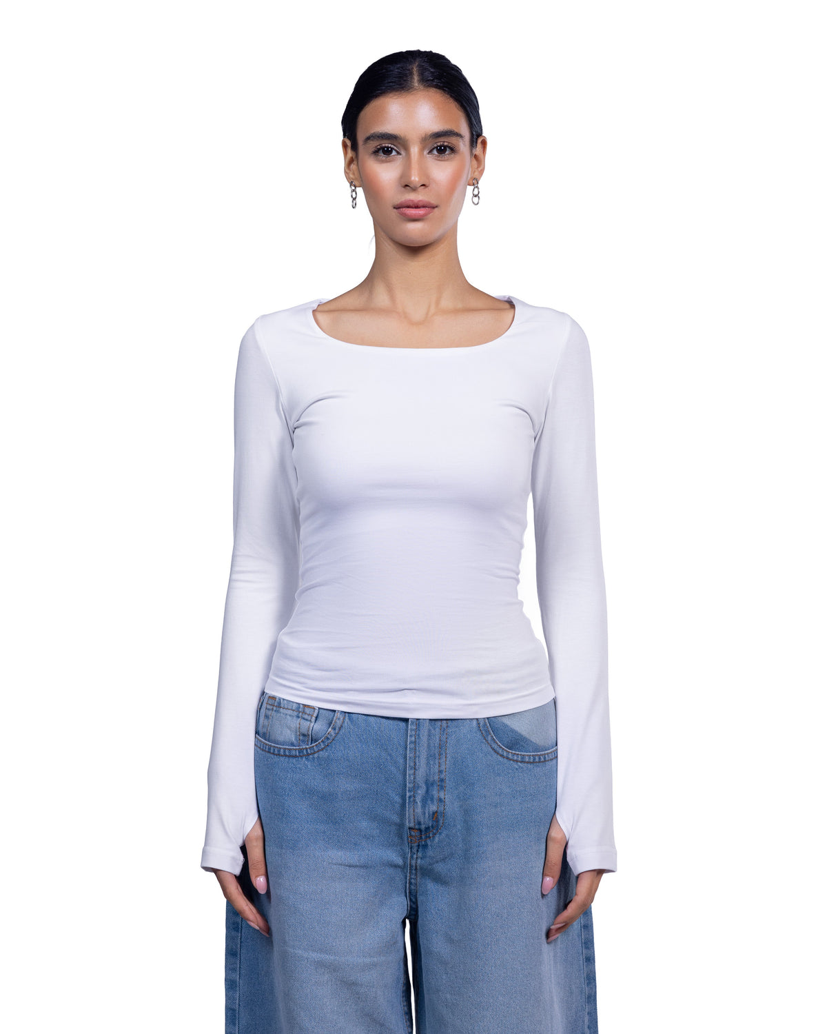 A woman modeling a fitted white long-sleeve top with a wide scoop neckline, paired with light blue jeans, against a plain white background.