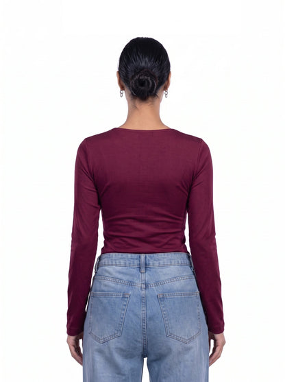 A woman viewed from the back wearing a fitted long-sleeve top in deep burgundy and light blue jeans, against a plain white background.
