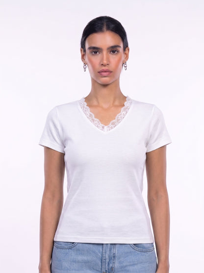 A woman modeling a white short-sleeve V-neck t-shirt with a delicate lace trim along the neckline, paired with light blue jeans against a plain white studio background.
