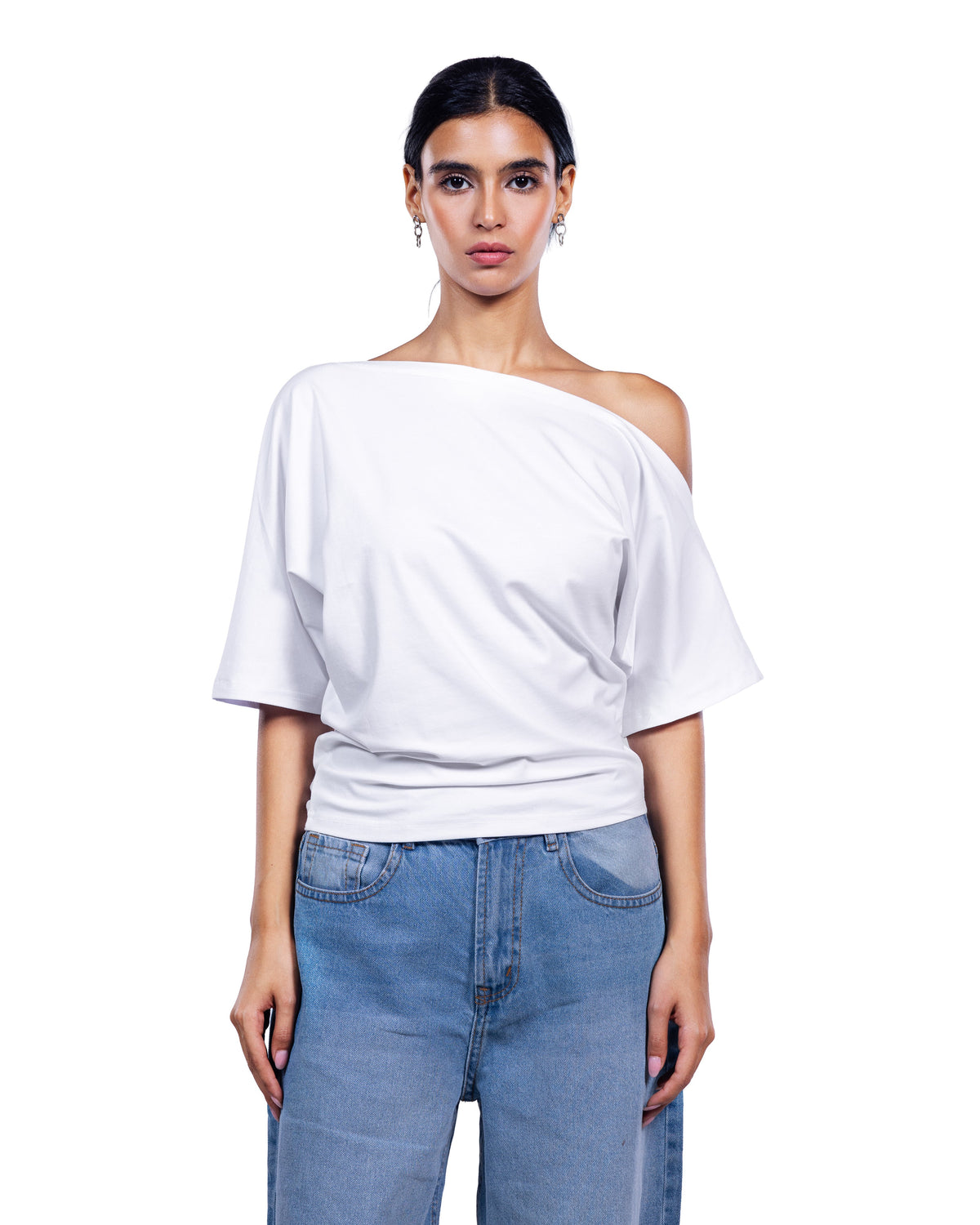 A woman modeling a white off-the-shoulder short-sleeve top paired with light blue jeans, shot against a solid white background.