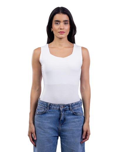 A woman modeling a white sleeveless scoop-neck tank top paired with blue jeans, shot against a solid white background.