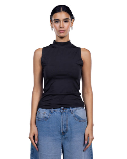 A woman modeling a sleeveless black mock neck top paired with light blue jeans against a plain white background.