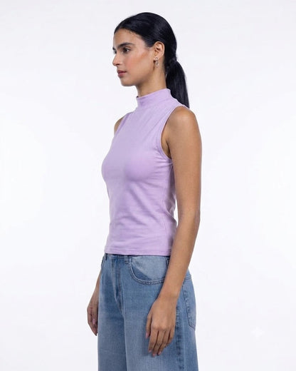 A woman in profile wearing a sleeveless lavender mock neck top and blue jeans, standing against a plain white studio background.