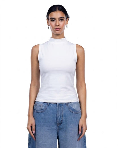 A woman modeling a white sleeveless mock neck top paired with light blue jeans against a plain white background.