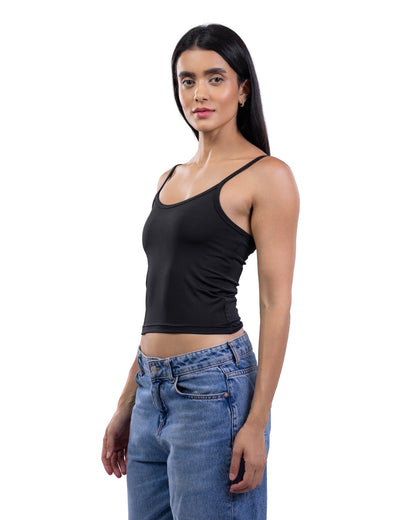 A woman modeling a black ribbed spaghetti-strap tank top paired with blue jeans, photographed against a solid white background.