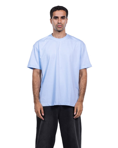 A man modeling a light blue crew-neck t-shirt and black pants against a plain white background.