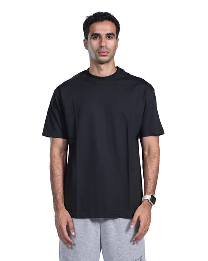 A man wearing a plain black short-sleeve crewneck t-shirt and light gray sweatpants, standing against a solid white background.