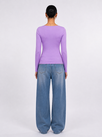 A model viewed from the back wearing a fitted lavender long-sleeve top and wide-leg blue jeans against a plain light gray studio background.